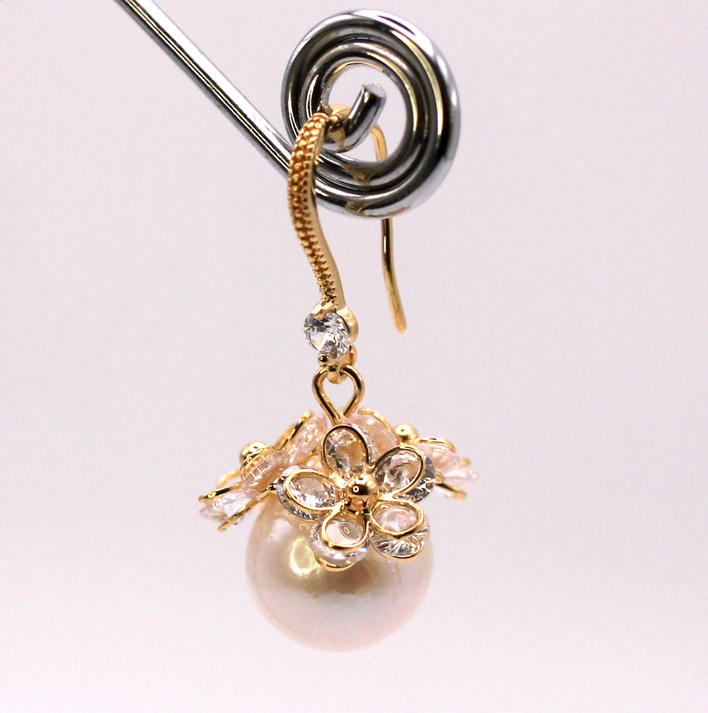 Women's Gold Plated Sterling Silver Earrings with Dangling 12 mm white round freshwater Pearls. The white pearl hangs at the bottom of a Sheppard hook set with zircon gemstones and a cluster of three crystal flowers.