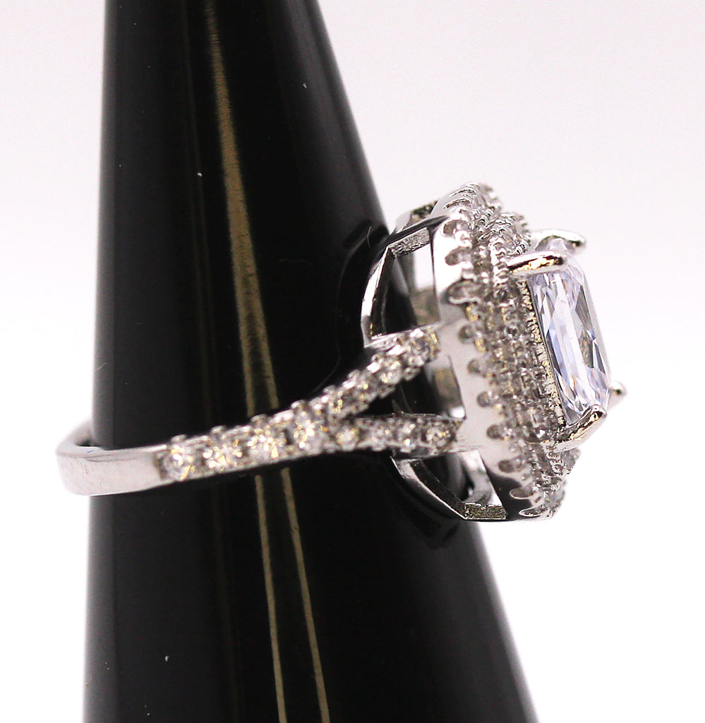 Women's Silver/Rhodium Plated Emerald Cut Solitaire Ring with Clear Zircon Gemstones. The solitaire is accented with two circles of pave set crystal stones on the face of the ring. The band is also accented with pave set zircons. Side view