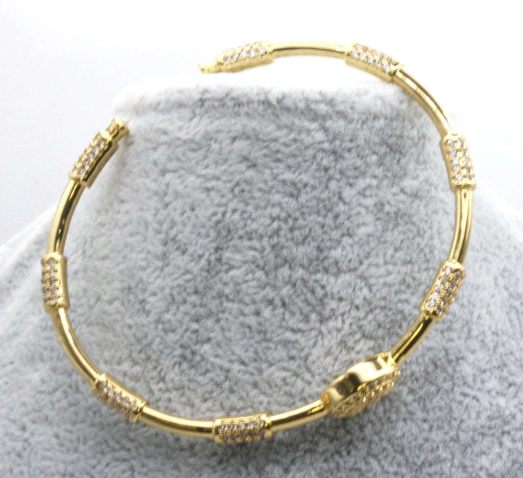Women's open bangle bracelet. Yellow gold plated. Decorated with cylinders pave set clear zircon gemstones.