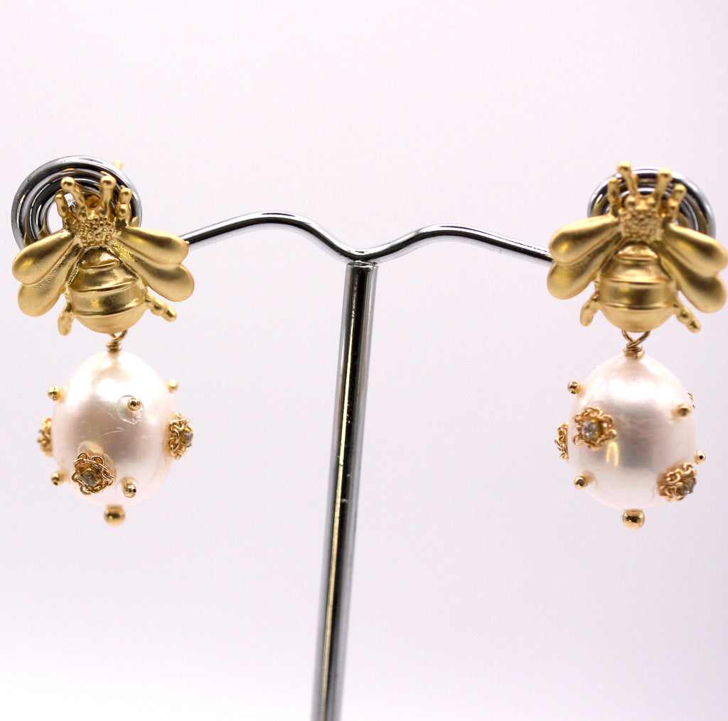 Genuine freshwater pearl earrings.  The 12 mm diameter white pearl is decorated with clear zircon gemstones. The pearl dangles below a gold plated sterling silver bumble bee post. Face view