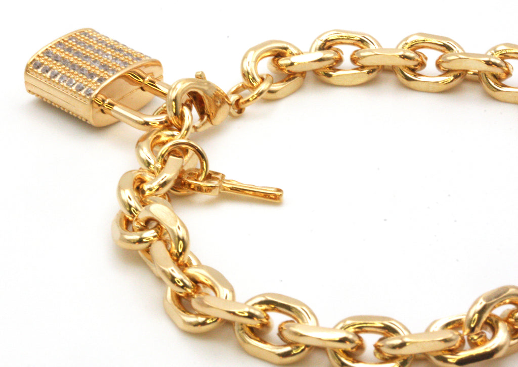 Women's bracelet. Chain links with a lock and key charm. The lock is pave set with clear zircon gemstones. Lobster claw closure. 7 inch length. Available in gold or silver/rhodium plating.