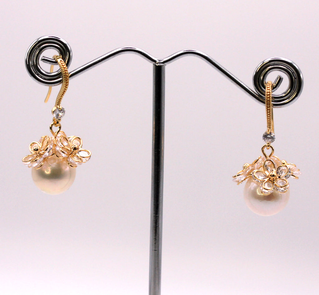 Women's Gold Plated Sterling Silver Earrings with Dangling 12 mm white round freshwater Pearls. The white pearl hangs at the bottom of a Sheppard hook set with zircon gemstones and a cluster of three crystal flowers. Face view