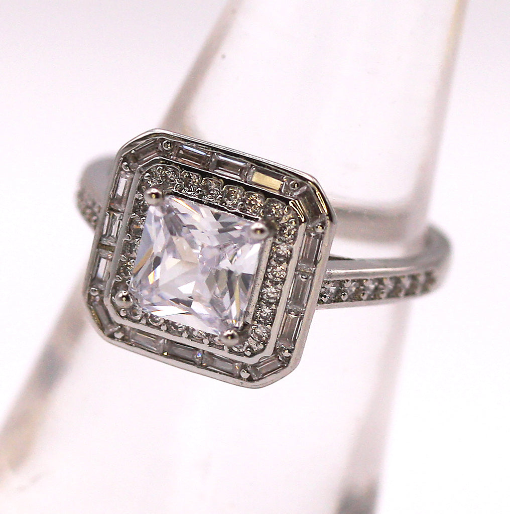 Women's Silver/Rhodium Plated Square Cut Solitaire Ring with Clear Zircon Gemstones. The solitaire is accented with one square of baguette cut crystals and on square of pave set crystal stones on the face of the ring. The band is also accented with pave set zircons.