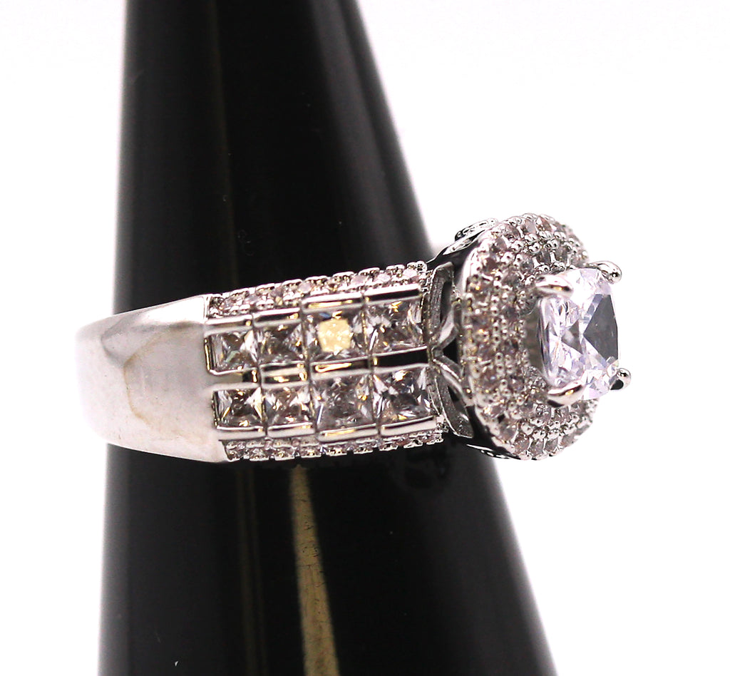Women's Silver/Rhodium Plated Square Cut Solitaire Ring with Clear Zircon Gemstones. The solitaire is accented with two circles of pave set crystal stones on the face of the ring. The band is also accented with eight square cut zircon crystals on each side of the ring. Side view